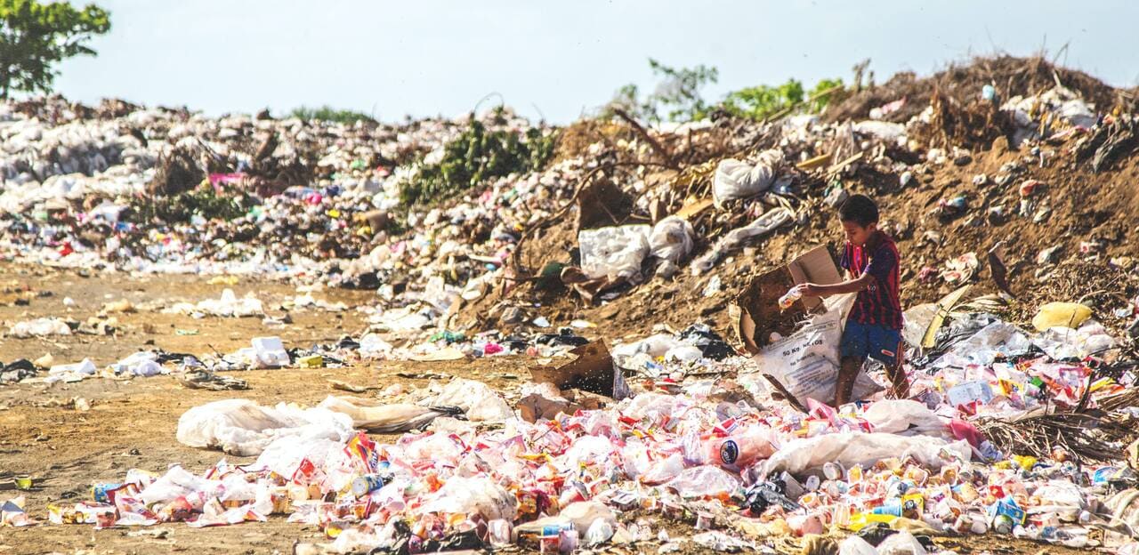 A young boy scavenging through a landfill filled with plastic waste, highlighting the human impact of unmanaged plastic pollution.