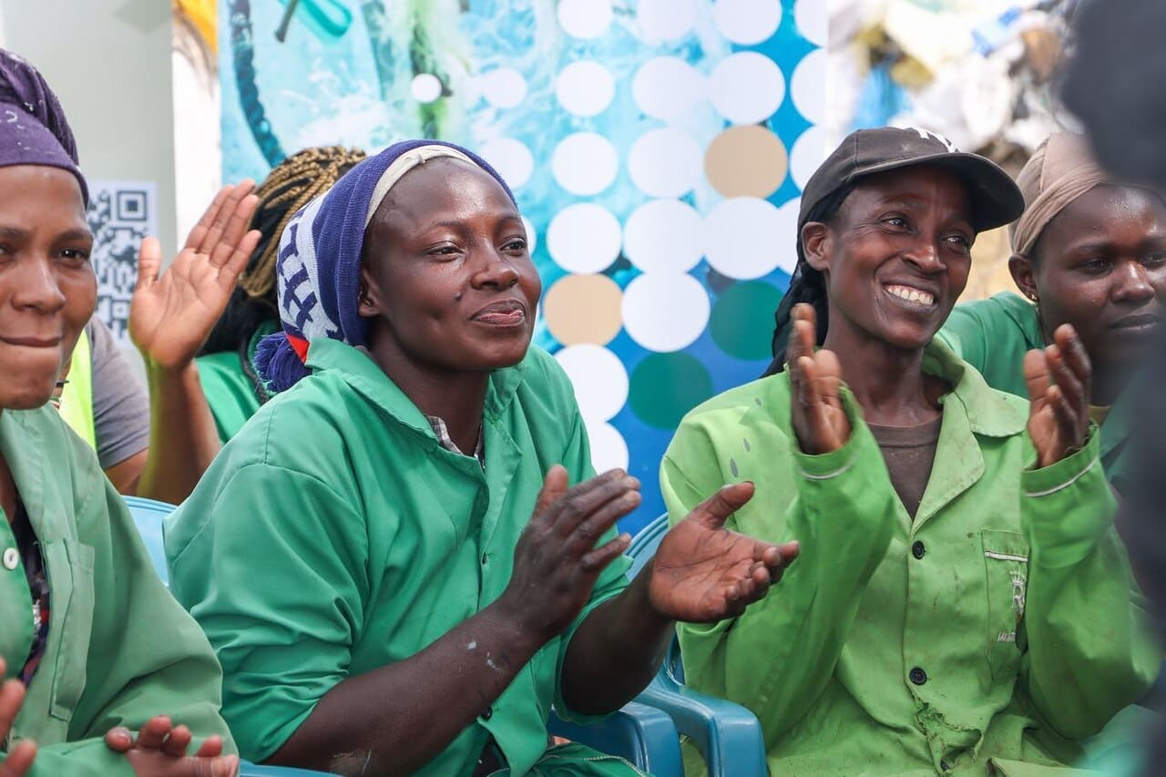 plastic waste workers wearing green gowns and clapping together and smiling