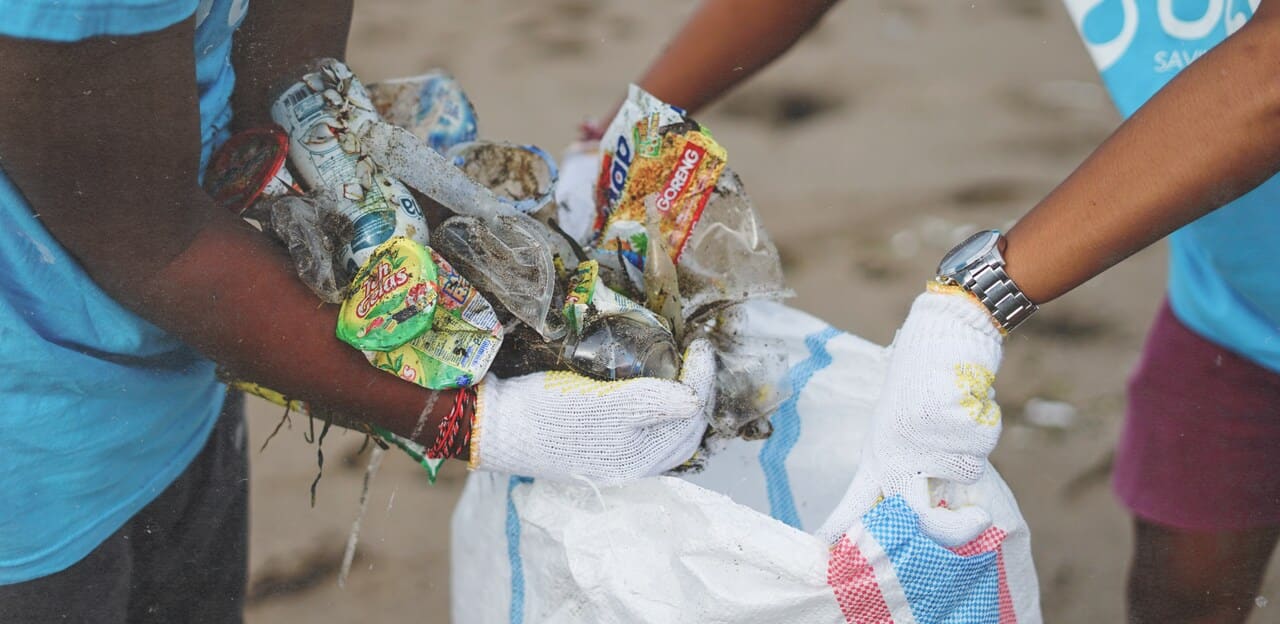 hands picking up plastic trash from the beach