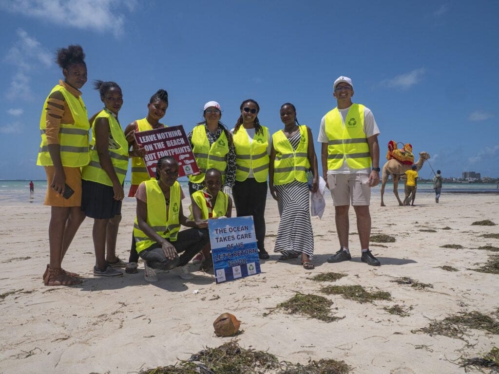 A group of volunteers wearing reflective vests poses on the beach in Mombasa, holding signs promoting eco-friendly practices during the International Coastal Cleanup.