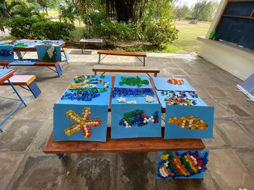 Art pieces made from upcycled bottle caps displayed on tables during the International Coastal Cleanup in Mombasa, highlighting creative recycling efforts.