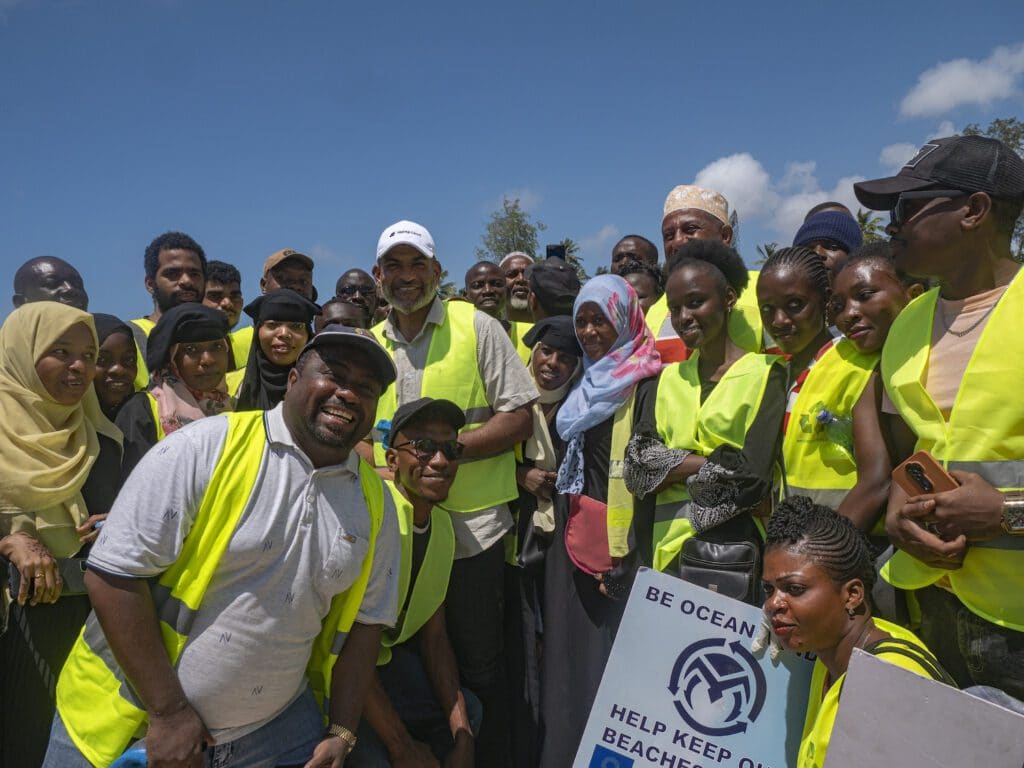 A large group of volunteers smiling and posing together in reflective vests after a successful cleanup effort on Mombasa’s coast.