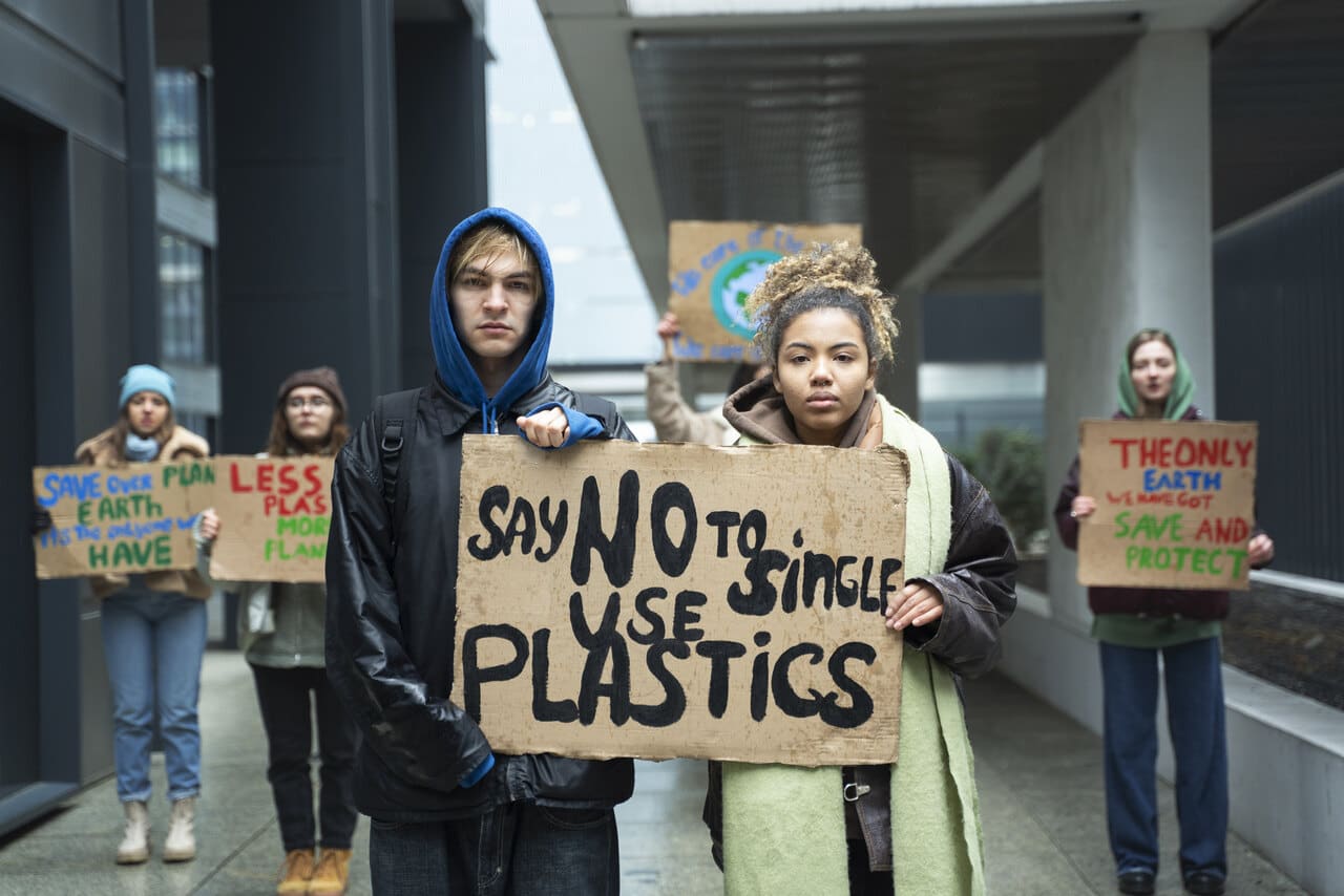 Young environmental activists protesting against plastic pollution, with a prominent sign reading 'Say No to Single-Use Plastics' and other signs promoting sustainability.